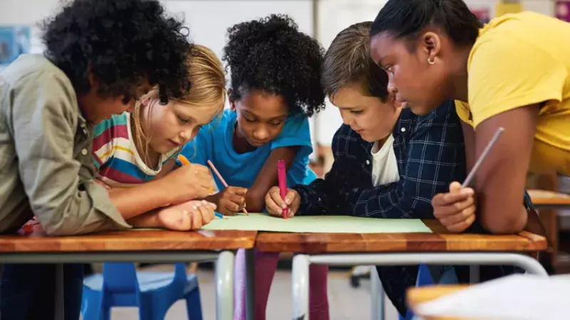 Photo d’un groupe diversifié d’enfants blottis les uns contre les autres et coloriant dans leur classe à l’école