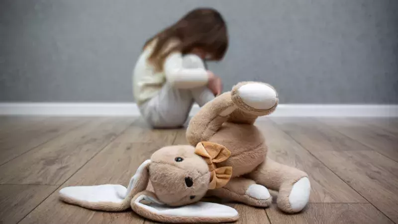 Petite-fille recroquevillée sur le sol avec premier plan sur son lapin en peluche.